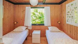 A room with wooden walls, two beds, a small white table, and a window with curtains. - Cozy home in Samsø with kitchen (Samsø)