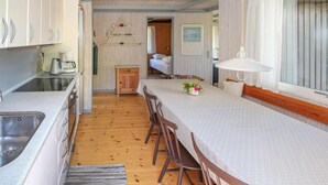 A compact kitchen with a sink, stove, and coffee maker. A dining area with a table and chairs is visible, leading to a bedroom with a bed and window. - Cozy home in Samsø with kitchen (Samsø)