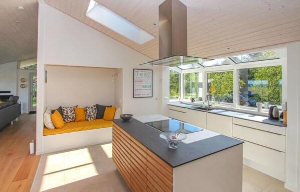 A modern kitchen with a central island, a built-in oven, and a window overlooking a garden. - Gorgeous home in Samsø with kitchen (Samsø)