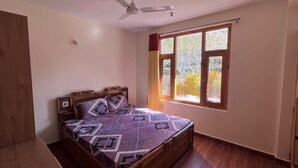 Ein Schlafzimmer mit Bett, Deckenventilator, Fenster mit Vorhängen und Holzboden.
