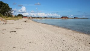 Una playa arenosa con un mar tranquilo, algunas personas y edificios al fondo.
