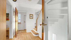 Ein Korridor mit Holzboden, weißen Wänden und einer Treppe mit Holzsitzstufen und einem Glasgeländer.