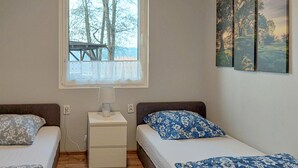 Une chambre avec deux lits, une table de chevet, une fenêtre donnant sur les arbres et trois tableaux encadrés accrochés au mur.
