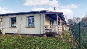 Une maison de plain-pied avec un porche, un petit jardin et une clôture en métal.