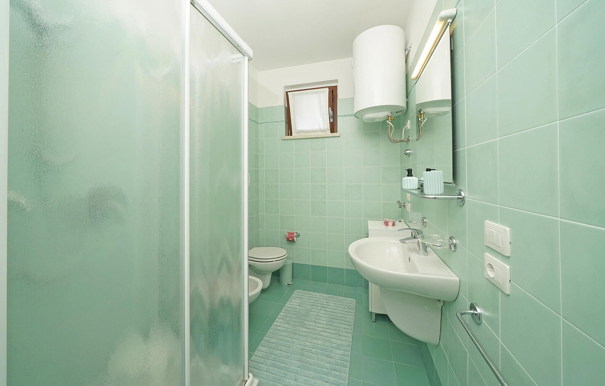 A bathroom with a shower, toilet, sink, and a small window.