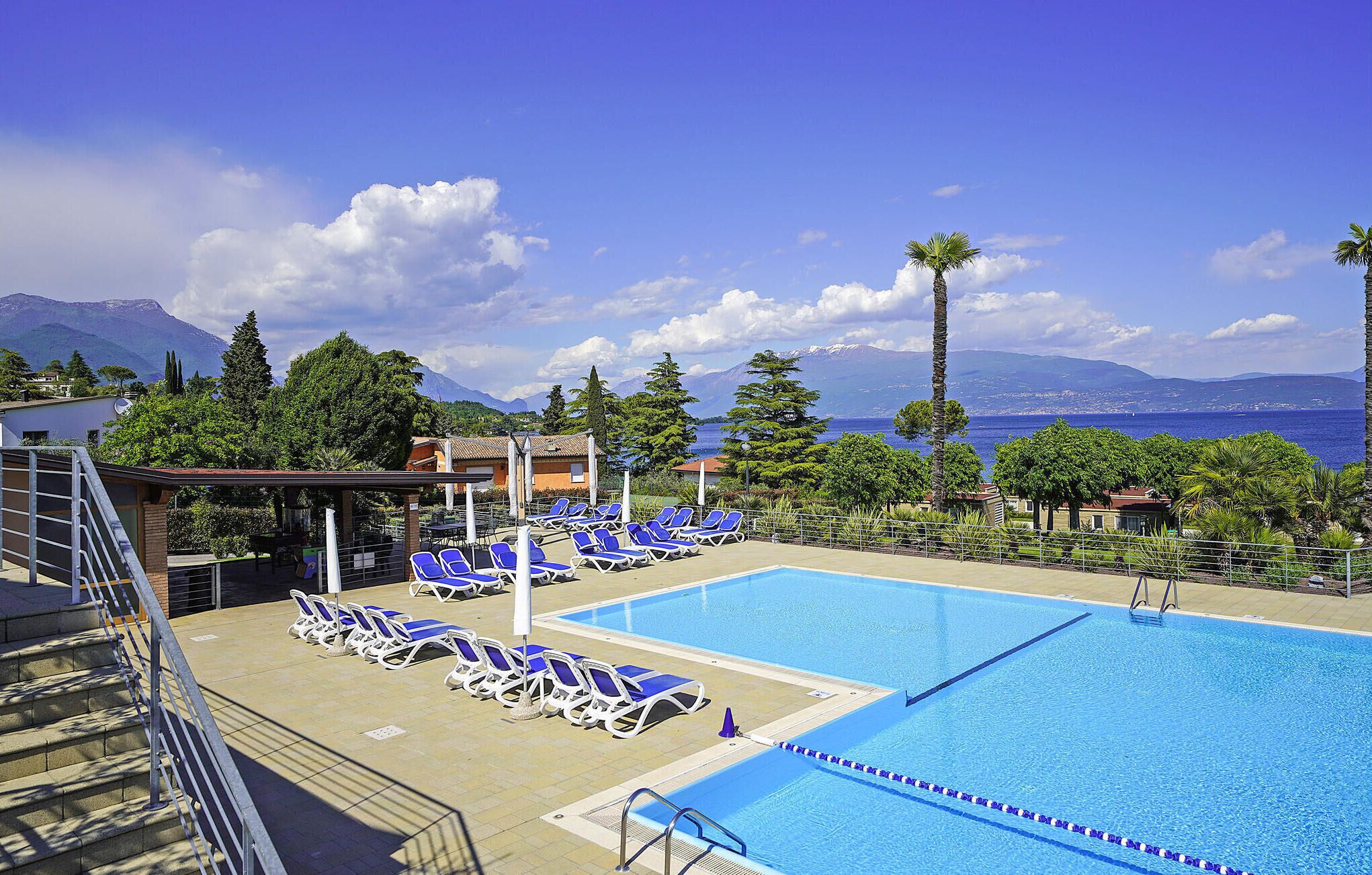 Un espace piscine avec des chaises longues bleues, un plongeoir et une vue sur la mer et les montagnes.