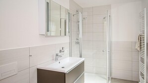 A modern bathroom with a glass shower enclosure, a white sink, and a towel rack.