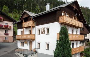 En traditionel træchalet med balkoner, en central trappe og et bjerg i baggrunden.