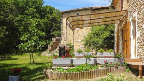 A stone building with a wooden deck and a pergola. There are flower beds with red flowers and a small tree. - 1 bedroom nice home in Dieulefit (Dieulefit)