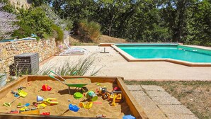 A backyard with a swimming pool, a sandbox, and a stone wall. - 1 bedroom nice home in Dieulefit (Dieulefit)