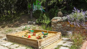 A sandbox with toys, a green playhouse, and a stone wall with lavender plants. - 1 bedroom nice home in Dieulefit (Dieulefit)