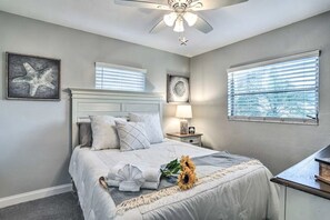 Une chambre à coucher comprenant un lit, une table de chevet, une lampe, un ventilateur de plafond et une fenêtre avec des stores.