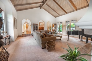 A spacious living room with a large sofa, a piano, and a dining area with a chandelier.