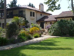 A two-story house with a tiled roof, a stone pathway, and a well-maintained garden with various plants and flowers.