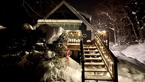 Un escalier recouvert de neige mène à une maison dotée d’un balcon, qui est elle-même entourée d’arbres et de neige.