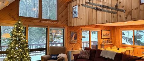 A cozy cabin interior with a large wooden ceiling, a Christmas tree, a couch, and a dining area.