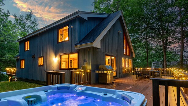 Une maison moderne dotée d’un jacuzzi sur la terrasse, entourée de guirlandes lumineuses et agrémentée d’une chaise longue.