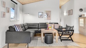 Un salon moderne avec un canapé d’angle, une petite table en bois, un fauteuil en cuir noir et un lampadaire.