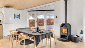 Une cuisine moderne équipée d’un poêle à bois, d’une table à manger avec des chaises et donnant, par de grandes portes vitrées, sur un jardin.