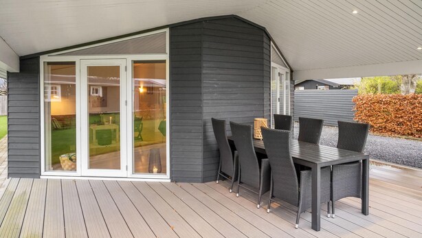 Une terrasse couverte avec une table et des chaises, une porte-fenêtre coulissante et une vue sur un jardin.