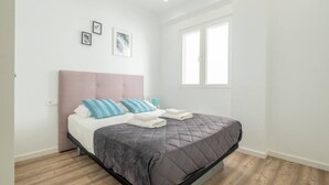 A modern bedroom with a large bed, a pink headboard, and a window with blinds. - Modern, Stylish Apartment with balcony (Valencia)