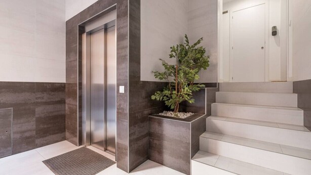 A modern elevator with a metallic finish, a potted plant beside a staircase, and a clean, minimalist design. - Modern, Stylish Apartment with balcony (Valencia)