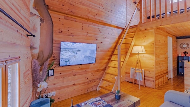 Een houten interieur met een aan de muur bevestigde televisie, een trap en een tafel met tijdschriften.
