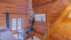 Een gezellig cabin interieur met houten wanden, een bank, een tafel met een plant en een aan de muur bevestigde televisie.
