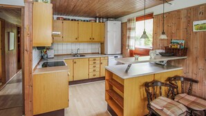 Keittiössä on puukehikoiset kaapit, jääkaappi, pesuallas sekä ruokailutila, jossa on pöytä ja tuolit.