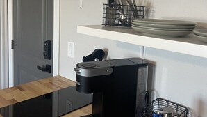 Une cuisine avec un plan de travail noir, une machine à café et des étagères au-dessus pour ranger la vaisselle et les ustensiles.