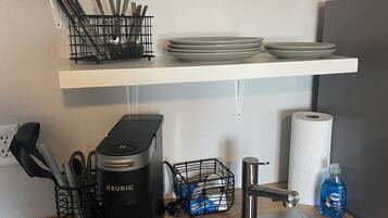 A kitchen with a coffee maker, a kettle, a sink, and various utensils on the counter.