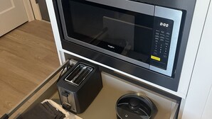 Une cuisine compacte équipée d’un four à micro-ondes, d’un grille-pain et d’un tiroir contenant une poêle et des ustensiles de cuisine.