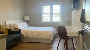 Une chambre avec un lit, un bureau, une chaise, un ventilateur de plafond et une fenêtre.