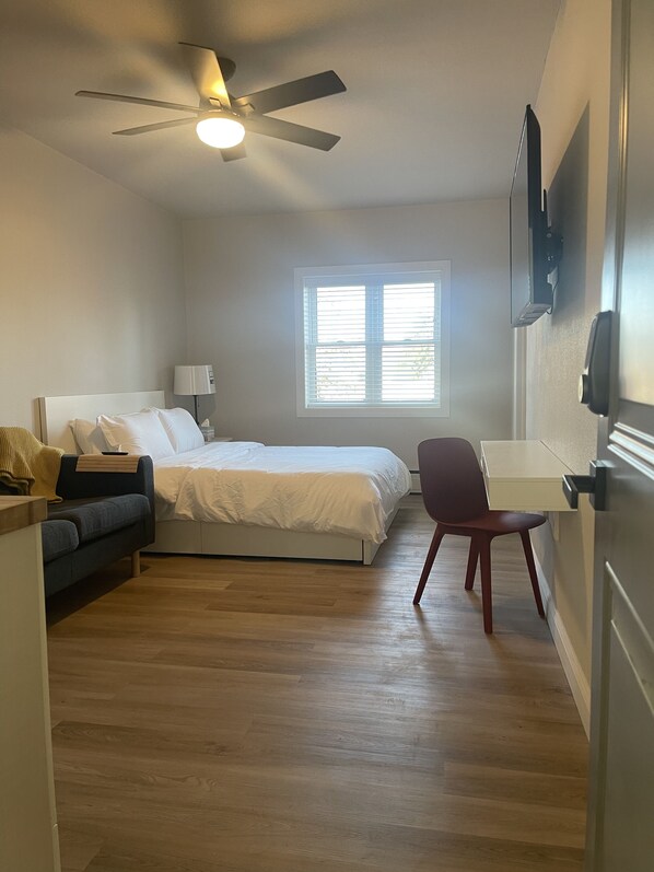 A bedroom with a bed, a desk, a chair, a ceiling fan, and a window.