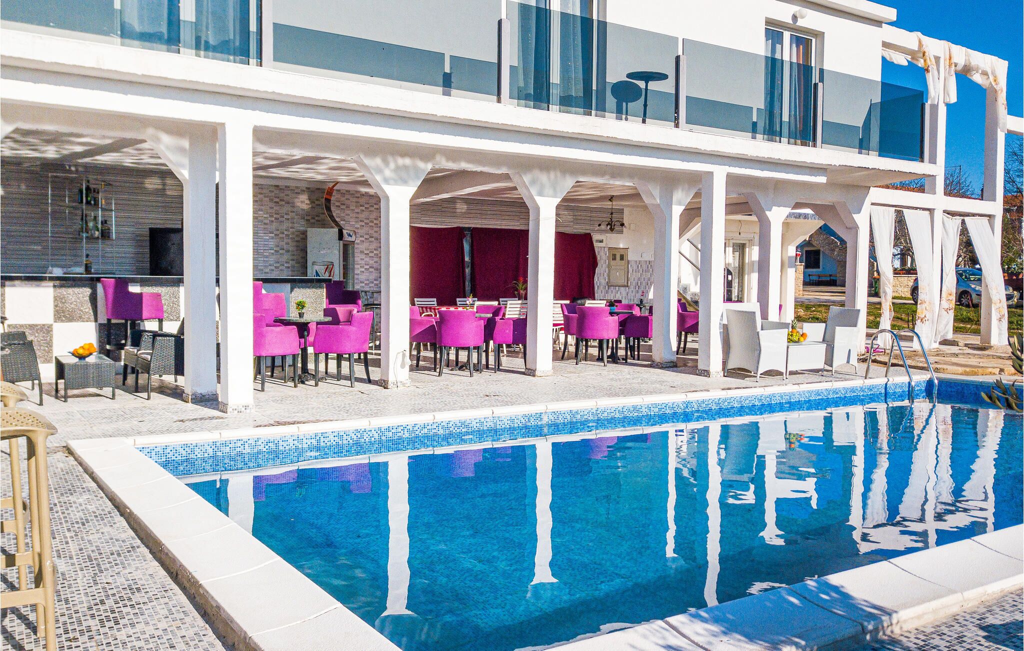 A poolside area with a clear blue pool, white columns, and pink chairs.