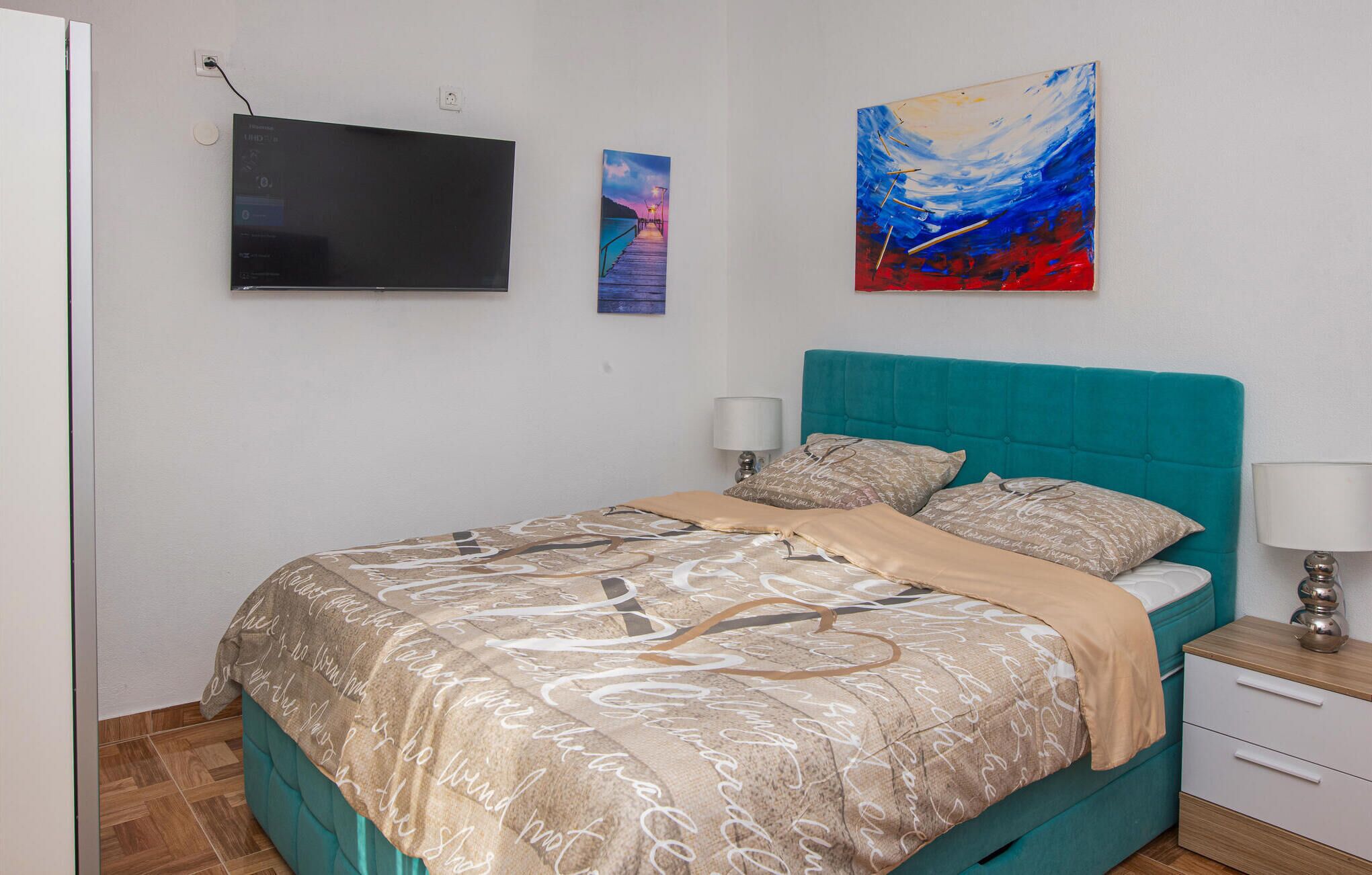 A bedroom with a bed, two bedside tables, a TV, and artwork on the wall.