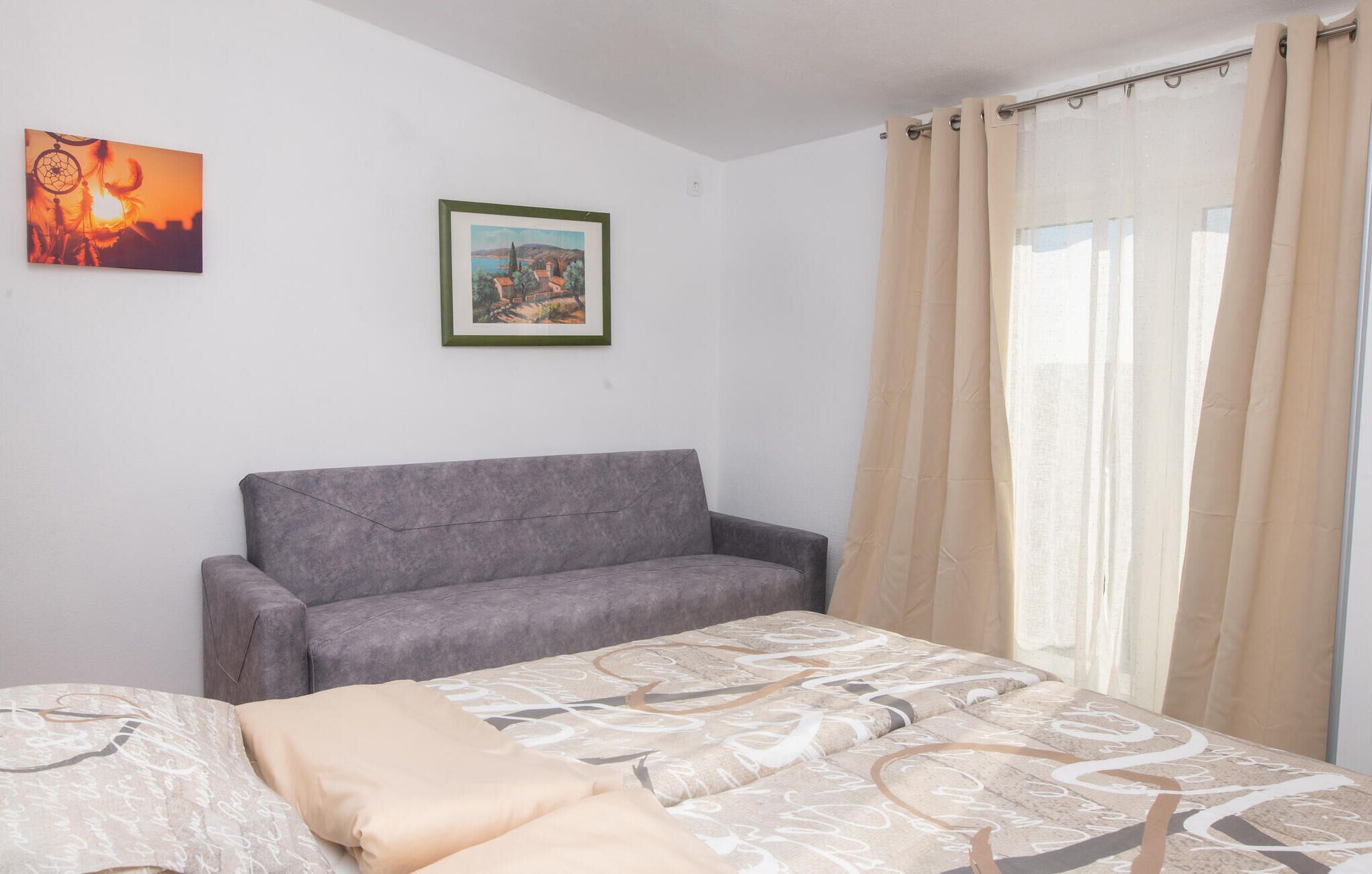 Une pièce avec un canapé gris, un lit recouvert d’une literie à motifs et deux tableaux encadrés accrochés au mur.