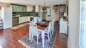 A modern kitchen with white cabinets, a dining area with a wooden table and white chairs, and a spiral staircase leading to an upper level.