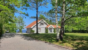A two-story house with a red roof, surrounded by trees and a gravel driveway.