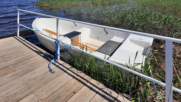 Een boot afgemeerd aan een houten steiger met een metalen hek, omgeven door water en begroeiing.