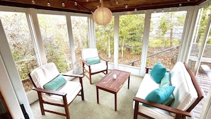 A covered patio with wooden furniture, including chairs and a sofa, and a hanging light fixture. - Sunny 3 bedroom cape with large deck, porch and kayaks. Pet friendly. (Oak Bluffs)