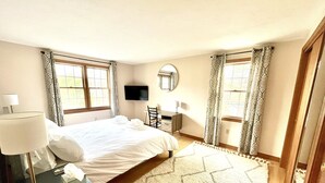 A bedroom with a bed, a desk, a chair, a TV, and a window with curtains. - Sunny 3 bedroom cape with large deck, porch and kayaks. Pet friendly. (Oak Bluffs)