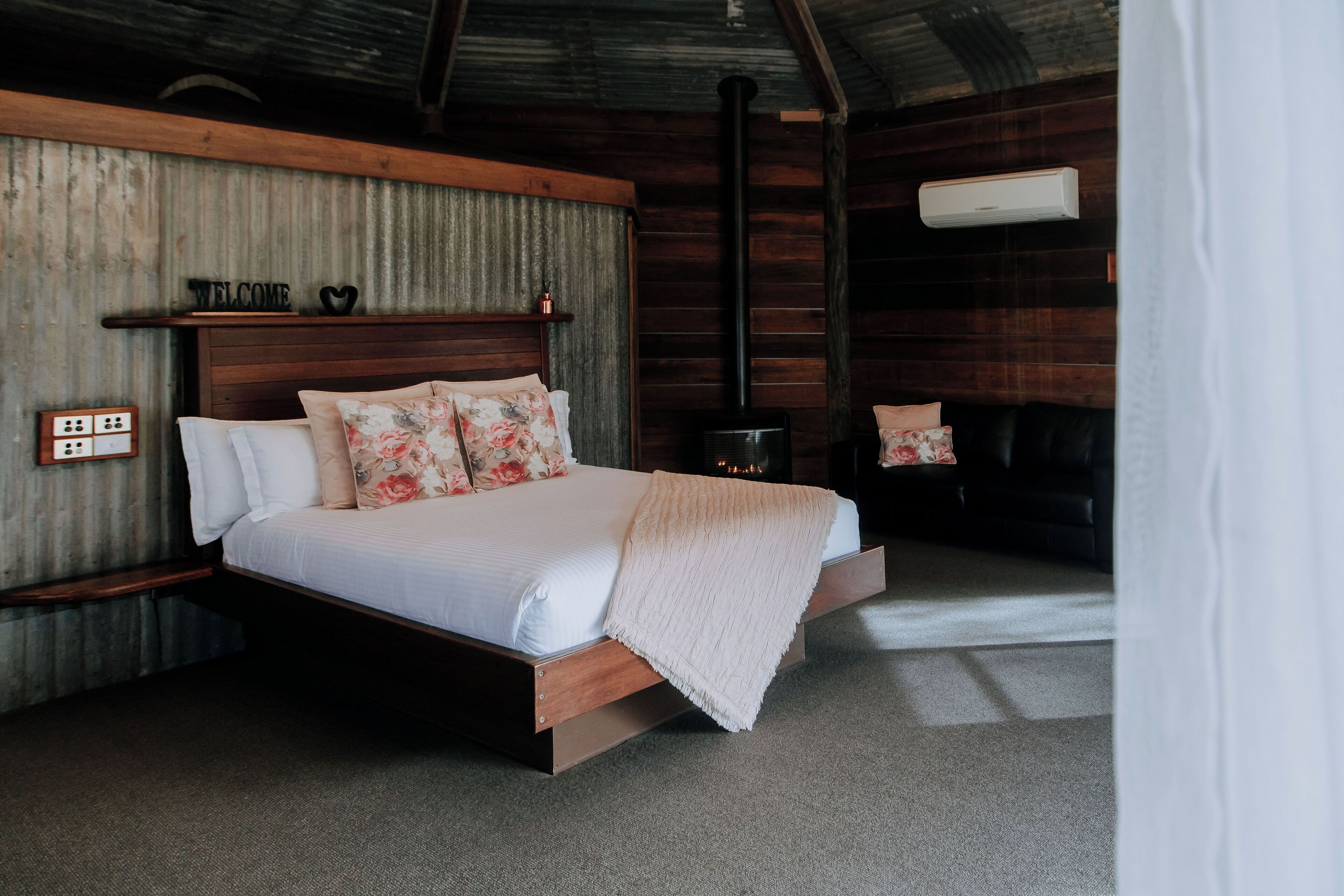 A bedroom with a wooden bed, a headboard, a bedside table, a nightstand, and a wall-mounted air conditioning unit.