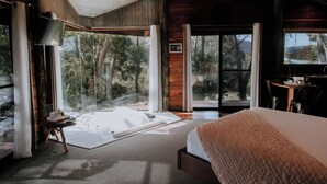 A bedroom with a large bed, a TV, and a sliding glass door leading to a balcony with a view of trees. - Eagle View Escape (Rydal)
