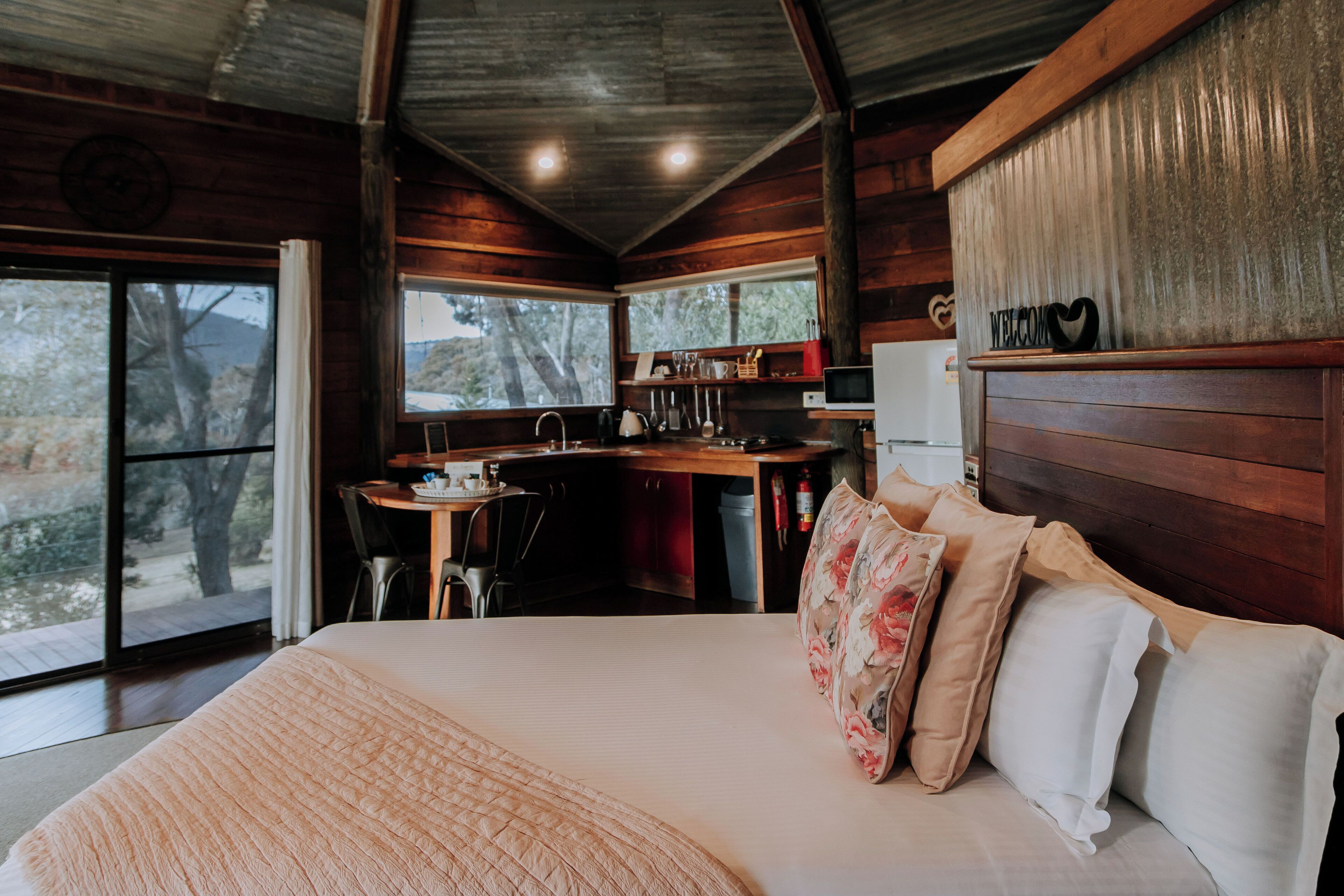 A cozy cabin-style room with a large bed, a wooden desk, and a kitchen area.