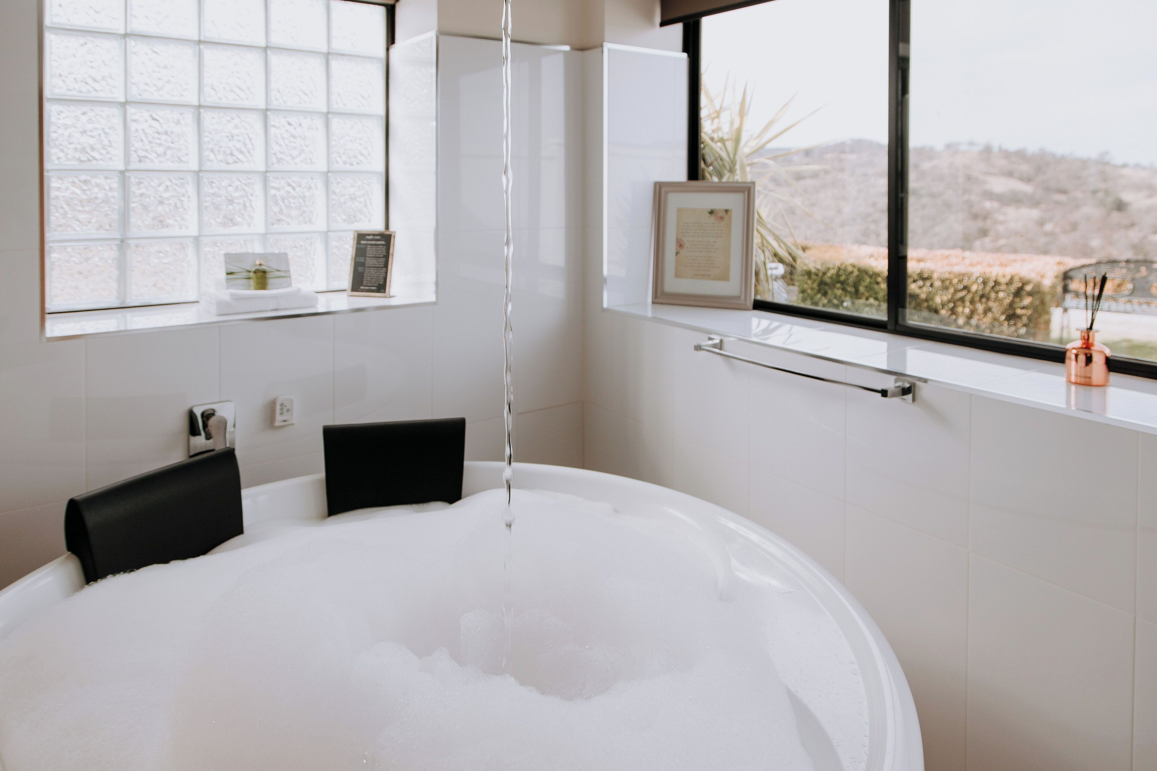 Un baño moderno con una bañera grande, una ventana que ofrece vistas a un paisaje montañoso y un estante con artículos de aseo.
