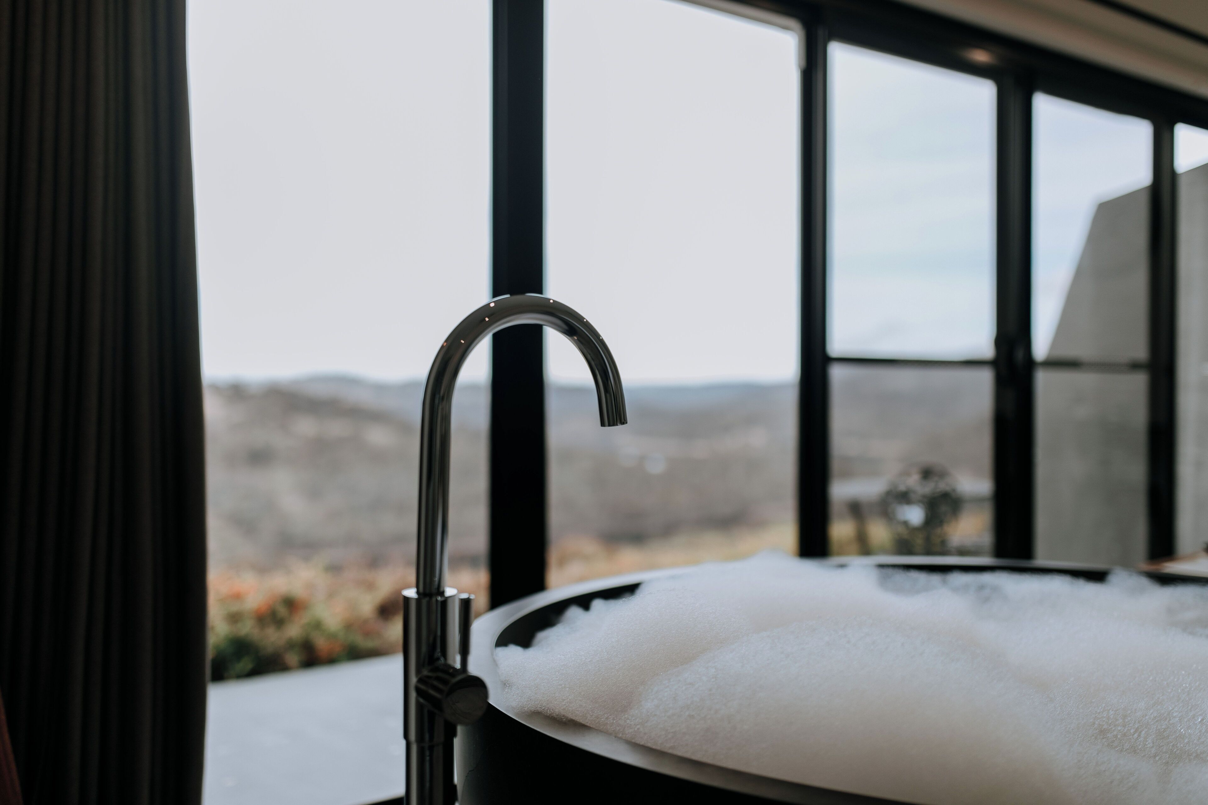 A bathtub with a view of a mountainous landscape through large windows.