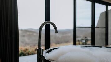 A bathtub with a view of a mountainous landscape through large windows.