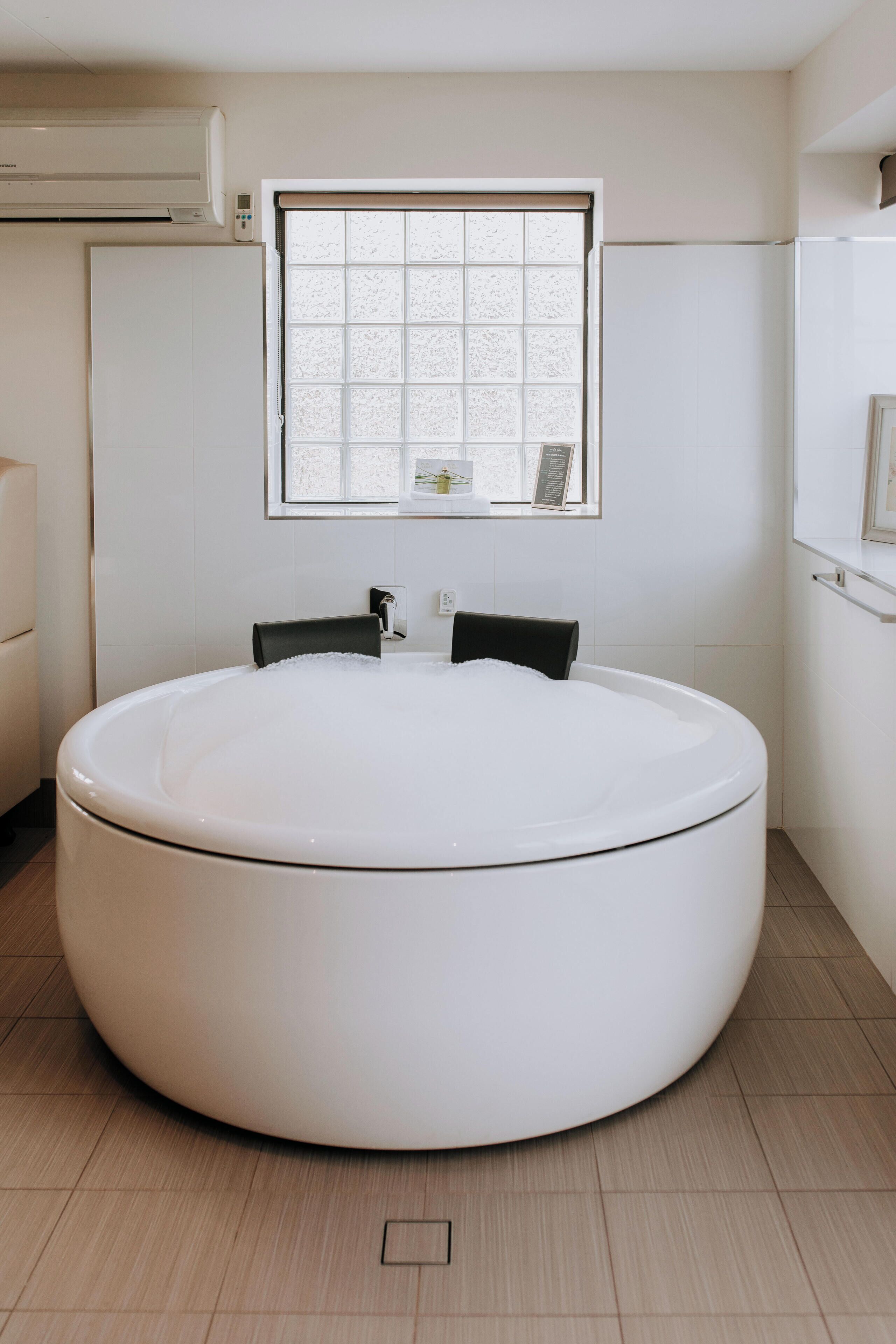 A modern bathroom with a large round bathtub, a window with a view, and a white toilet.