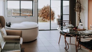 A modern living room with a glass table, leather sofa, and a large window with a view of a tree and hills. - Eagle View Escape (Rydal)